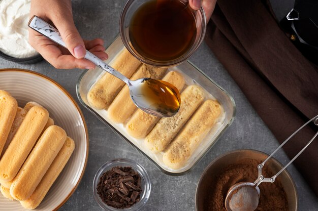 Top view hand pouring coffee over ladyfingers