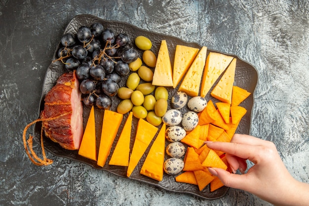 Top view of hand taking one of foods from delicious best snack for wine on brown tray on ice background
