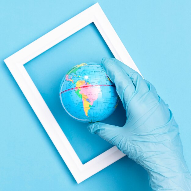 Top view of hand with surgical glove holding earth globe in frame