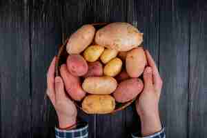 Free photo top view of hands holding basket with potatoes on wooden surface