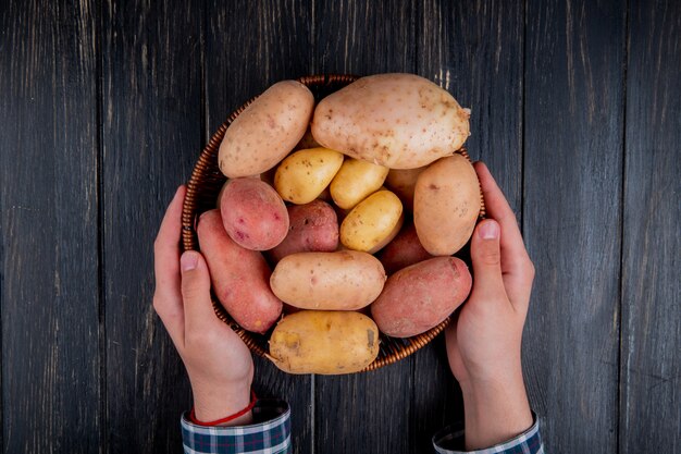 Top view of hands holding basket with potatoes on wooden surface