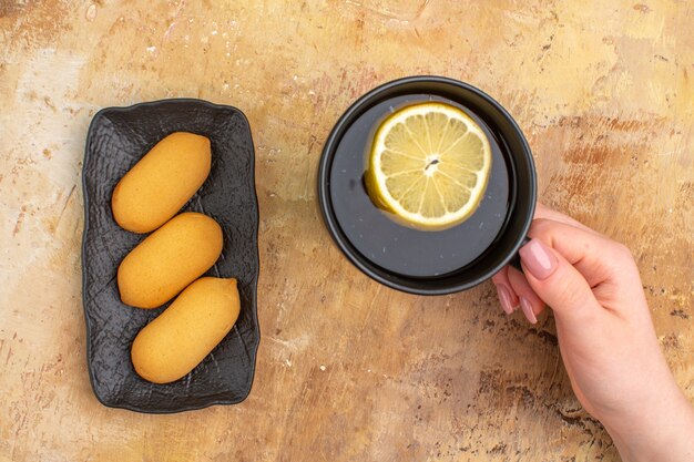混合色の背景にレモンとビスケットとカップで紅茶を保持している手の上面図