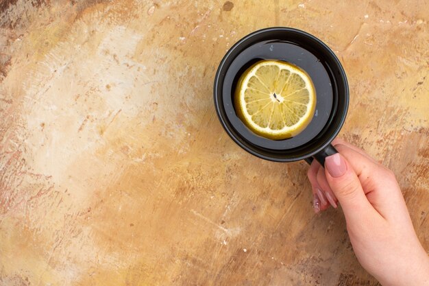 Top view of hands holding black tea in a cup with lemon on mixed color background