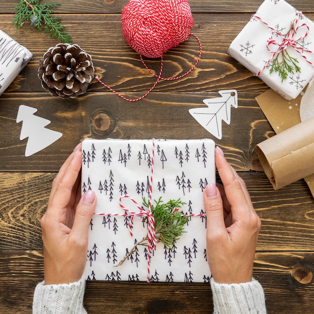 Free photo top view of hands holding christmas gift with pine cone and string