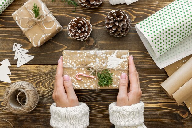 Top view of hands holding christmas gift with string and pine cones