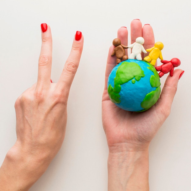 Top view of hands holding plasticine globe and people and making peace sign