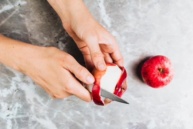 Free photo top view of hands peeling an apple on marble background