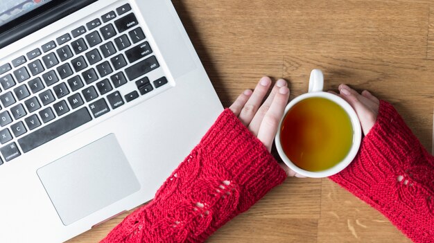 Top view of hands with cup of tea and laptop