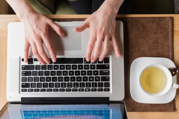 Top view of hands with laptop next to a tea cup