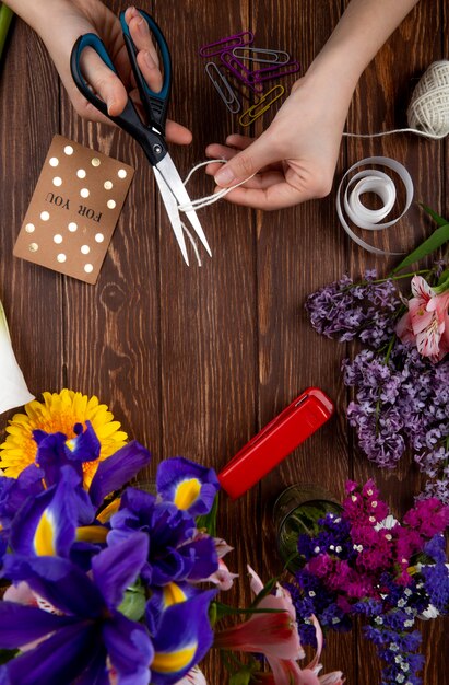 Вид сверху руки с ножницами резки каната открытки скрепки и букет фиолетовых ирисов на деревянных фоне