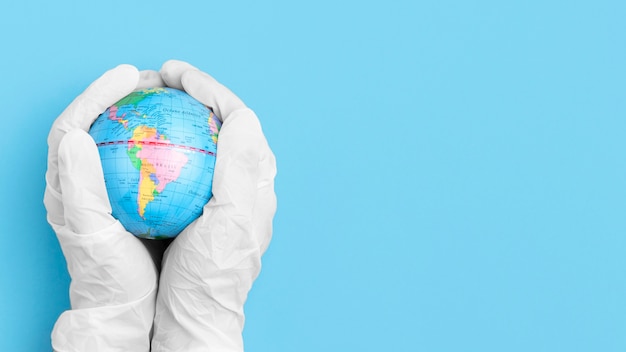 Free photo top view of hands with surgical gloves holding globe with copy space