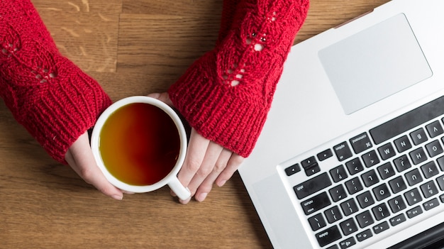 Foto gratuita vista dall'alto delle mani con la tazza di tè accanto a un computer portatile