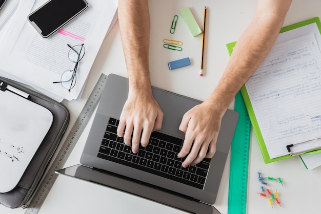 Free photo top view hands working on laptop surrounded by stationery elements