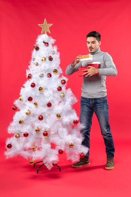 Top view of handsome adult in a gray blouse standing near the decorated white Christmas tree