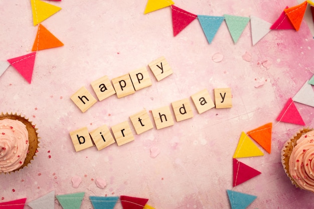 Top view of happy birthday wish in wooden letters with garlands and cupcakes