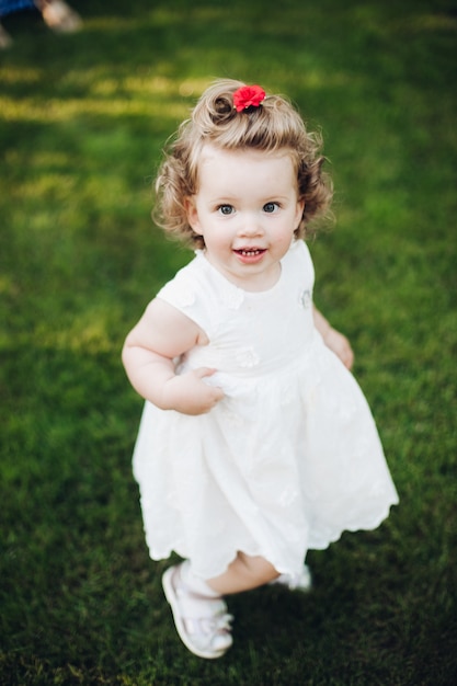 Top view of happy cute toddler girl with curly hair standing in the garden and looking at the camera