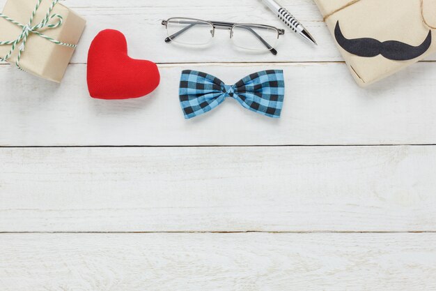 Top view Happy Father day.accessories with red heart,mustache,vintage bow tie,present,pen on rustic white wooden background.