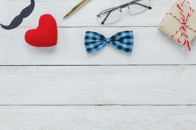 Top view Happy Father day.accessories with red heart,mustache,vintage bow tie,present,pen on rustic white wooden background.