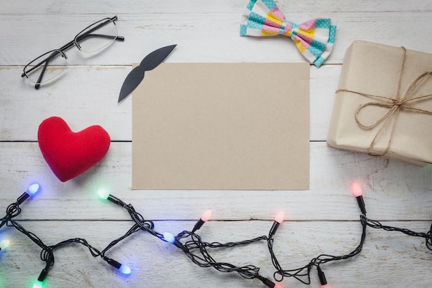 Top view happy father day.blank paper for free text space on rustic wooden background.accessories with ,lights,gift,mustache,vintage bow tie,eyeglasses,present,red heart.