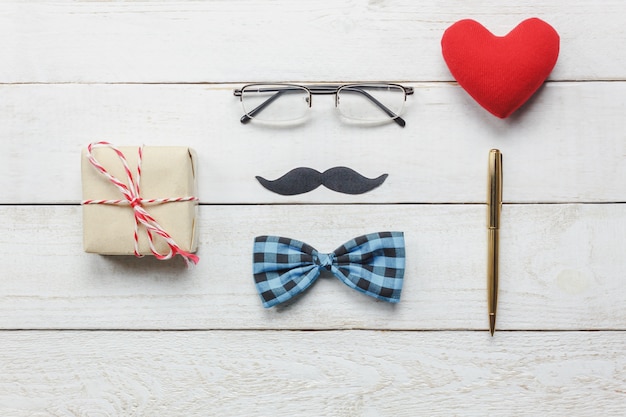 Top view Happy Father day.flat lay accessories with red heart,mustache,vintage bow tie,present,pen on rustic white wooden background.