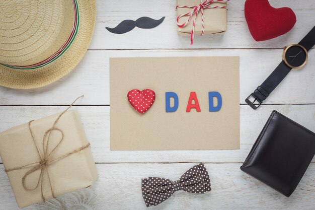 Top view Happy Father day .Red heart and word "DAD" on paper.accessories with mustache,vintage bow tie,wallet,hat,present and watch rustic wooden background.