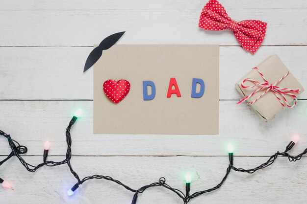 Top view Happy Father day.Red heart and word "DAD" on rustic wooden background.accessories with paper,lights,gift,mustache,vintage bow tie present and tree.