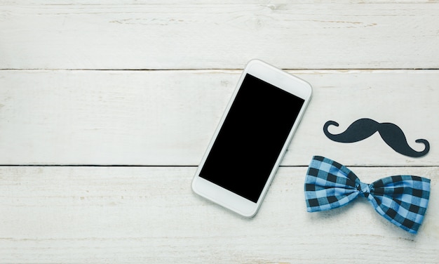 Top view Happy Father day.White mobile phone on rustic wooden background.Sign father is mustache and vintage bow tie.