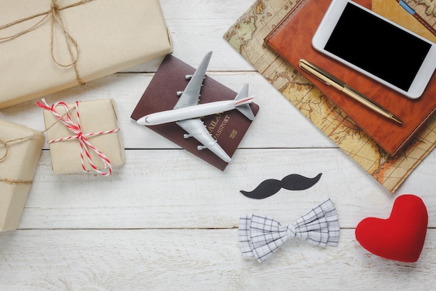 Top view Happy Father day with travel.Airplane and passport on rustic wooden background.accessories with ,map,mustache,vintage bow tie,pen,present,red heart,white mobile phone and notebook.