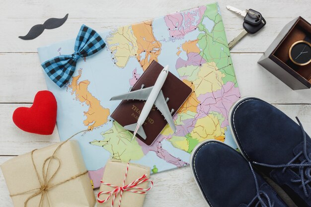 トップビュー旅行のコンセプトを持つ幸せな父の日。地図と素朴な木製の背景に飛行機とパスポート。赤い心臓のアクセサリー、口ひげ、ヴィンテージの蝶ネクタイ、キー、プレゼント、靴、時計。