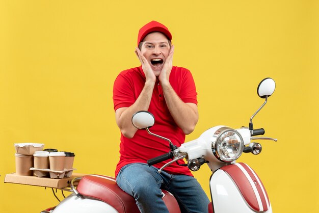 Top view of happy smiling young adult wearing red blouse and hat delivering order sitting on scooter on yellow background