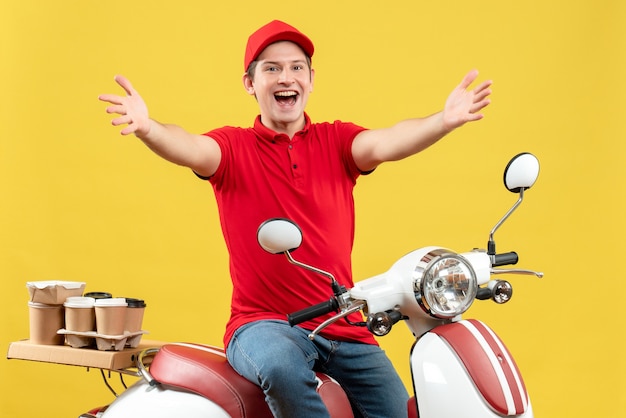 赤いブラウスと帽子を身に着けている幸せな若い大人の平面図黄色の背景に腕を前方に伸ばしてスクーターに座って注文を配信します。