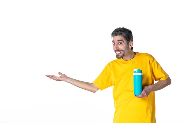노란색 셔츠를 입고 흰색 배경의 오른쪽에 있는 무언가를 가리키는 파란색 보온병을 보여주는 행복한 젊은 남성의 상위 뷰