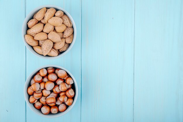 Top view of hazelnuts and almond in shell in bowls on blue wooden background with copy space