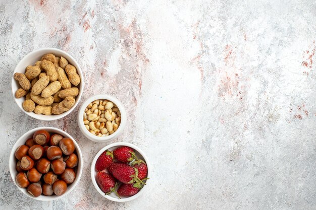 Top view of hazelnuts and peanuts with strawberries on a white surface