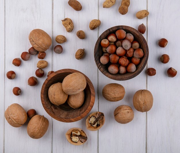 Top view of hazelnuts with walnuts and peanuts in bowls on a white surface