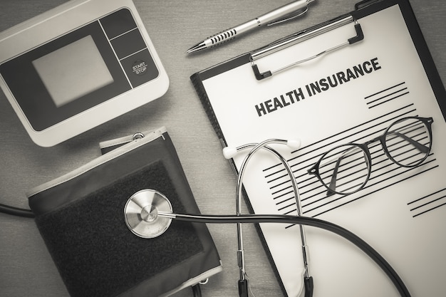 Top view health insurance form eyeglasses and pulse gauge with stethoscope on wooden background.