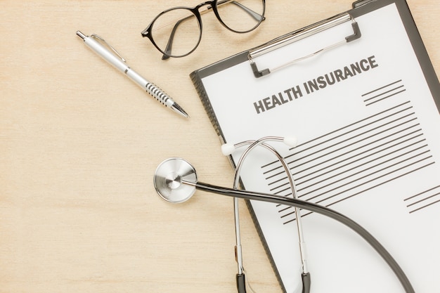 Free photo top view health insurance form and eyeglasses with stethoscope on wooden background.business and healthcare concept.savings.flat lay.copy space.