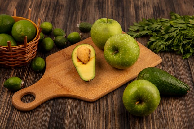 Top view of healthy apples on a wooden kitchen board with limes on a bucket with feijoas avocados and parsley isolated on a wooden surface