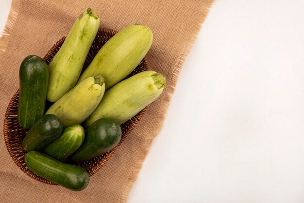 コピースペースと白い背景の上の袋布のバケツにキュウリズッキーニなどの健康的な緑の野菜の上面図