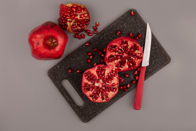 Top view of healthy halved pomegranates on a black kitchen board with knife with whole pomegranates isolated