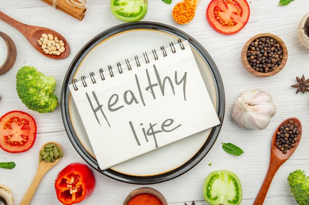 Top view healthy life written on notepad on plate with green tomato and black pepper on grey table