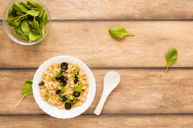 Top view of healthy oats garnished with basil leaf and olive in bowl on wooden table
