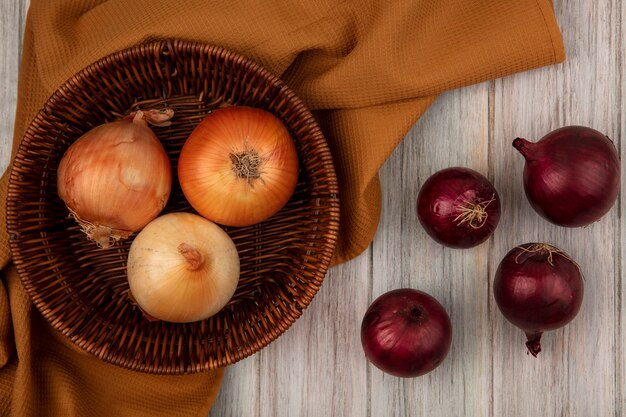 Top view of healthy onions on a bucket on a cloth with red onions isolated on a grey wooden surface