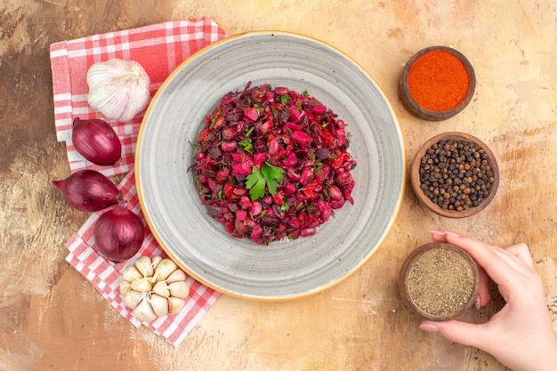 Top view healthy red salad on a gray plate with black pepper ground black pepper turmeric on the right and three red onions garlic on the left on a wooden background