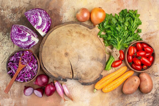Вид сверху здоровые ингредиенты салата, сделанные из пучка красной капусты, помидоров рома, петрушки, моркови, картофеля и лука вокруг разделочной доски на деревянном столе с копией пространства