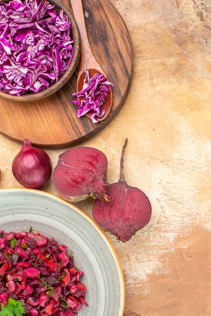 Top view healthy salad with green leaves on it with bowl of chopped cabbage onion and beetroots on a light wooden table with copy place