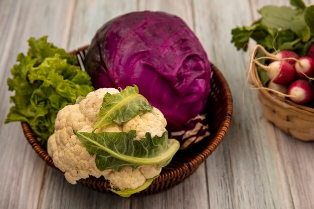 Top view of healthy vegetables such as cauliflower purple cabbage and lettuce on a bucket with radishes on a bucket on a grey wooden surface