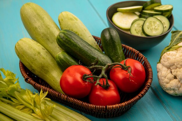 Top view of healthy vegetables such as tomatoes cucumbers and zucchinis on a bucket with cauliflower and celery isolated on a blue wooden wall