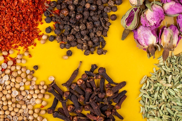 Top view of heaps of spices and herbs on a yellow background