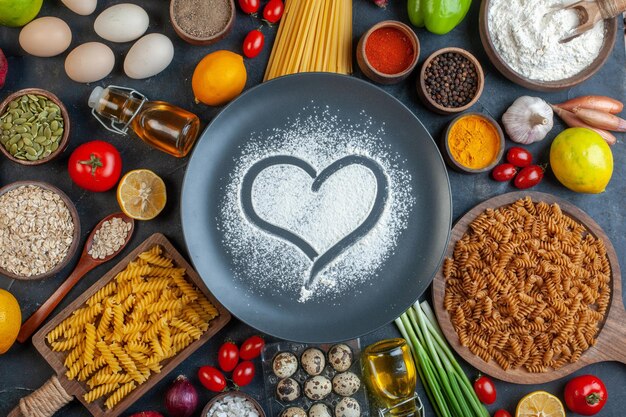 上面図ハート型小麦粉の周りの卵トマト調味料と暗い背景のイタリアンパスタ果物野菜料理食事色料理